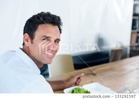 Middle-aged man smiling and sitting at wooden table with takeout salad and water glass, copy space Middle-aged man smiling and sitting at wooden table with takeout salad and water glass, copy space 133291597