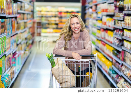 Woman smiling, pushing cart in store aisle with paper bag of green onions, baguette, wine bottle Woman smiling, pushing cart in store aisle with paper bag of green onions, baguette, wine bottle 133291604