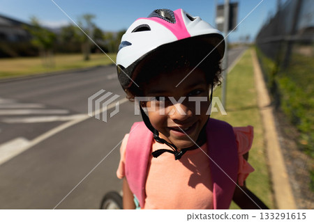 African American girl standing on suburban sidewalk wearing white-pink bicycle helmet and backpack 133291615