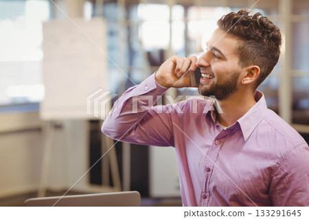 Man wearing shirt and talking on smartphone at office desk with laptop, flip chart, copy space Man wearing shirt and talking on smartphone at office desk with laptop, flip chart, copy space 133291645