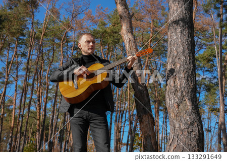 Blonde man playing string guitar outdoors in autumn forest. Concept of sound therapy, mental health and wellness rituals. Calmness tranquility audio-sensory practices. Aura farming energy Blonde man playing string guitar outdoors in autumn forest. Concept of sound therapy, mental health and wellness rituals. Calmness tranquility audio-sensory practices. Aura farming energy 133291649