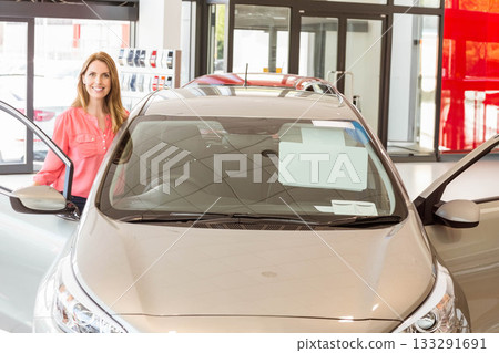 Mid-30s woman inspecting price sheet on silver hatchback windshield at showroom near sample rack Mid-30s woman inspecting price sheet on silver hatchback windshield at showroom near sample rack 133291691