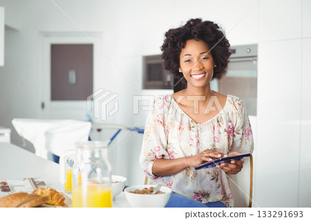 African American woman sitting at kitchen table holding tablet device by cereal bowls, copy space African American woman sitting at kitchen table holding tablet device by cereal bowls, copy space 133291693