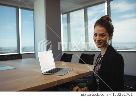 Woman wearing dark blazer working on laptop at conference room table with office chairs, copy space 133291701
