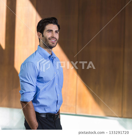 Man standing in lobby by wood panel wall wearing black leather belt, button-up shirt, copy space 133291720