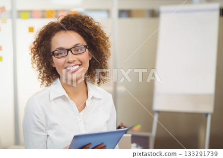 Smiling businesswoman holding tablet and standing by flip chart with sticky notes in meeting room 133291739