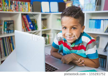 Hispanic child boy leaning on table in study room studying on silver laptop and turquoise binder Hispanic child boy leaning on table in study room studying on silver laptop and turquoise binder 133291752