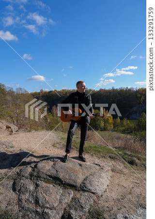 Blonde man playing string guitar outdoors in autumn forest. Concept of sound therapy, mental health and wellness rituals. Calmness tranquility audio-sensory practices. Aura farming energy 133291759