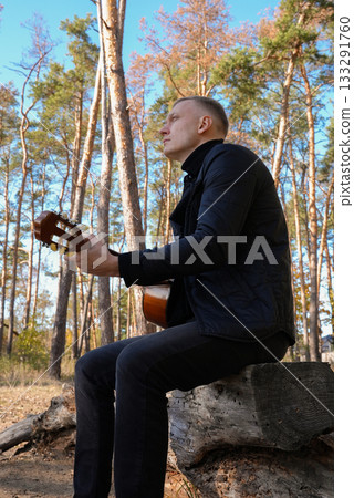 Portrait of smiling caucasian artist plays wooden acoustic guitar in autumnal park. Young songwriter plays string musical instrument hobby outside in nature fall time. Audio music healing Portrait of smiling caucasian artist plays wooden acoustic guitar in autumnal park. Young songwriter plays string musical instrument hobby outside in nature fall time. Audio music healing 133291760