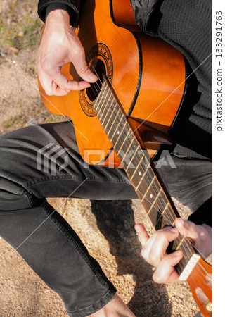 Close up hands of artist plays wooden acoustic guitar in autumnal park. Young songwriter plays string musical instrument hobby outside in nature fall time. Audio music healing Close up hands of artist plays wooden acoustic guitar in autumnal park. Young songwriter plays string musical instrument hobby outside in nature fall time. Audio music healing 133291763
