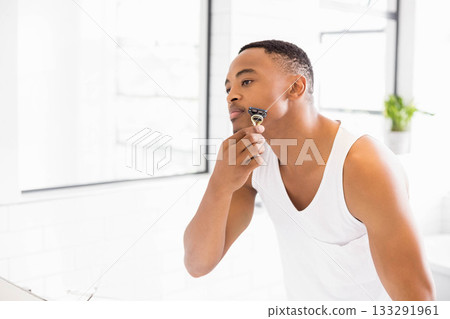 African American man shaving face at bathroom sink in front of mirror with handheld safety razor 133291961