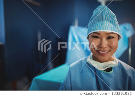 Asian female surgeon standing right of draped table in operating room wearing scrub cap, copy space 133291985