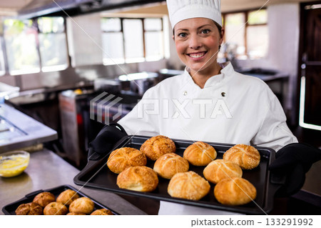 Female chef holding baking tray with sesame-topped bread rolls in commercial kitchen, copy space 133291992