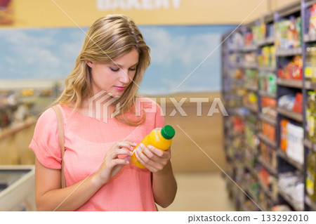 Fair-skinned woman checking label on orange juice bottle in bakery aisle near refrigerated counters Fair-skinned woman checking label on orange juice bottle in bakery aisle near refrigerated counters 133292010