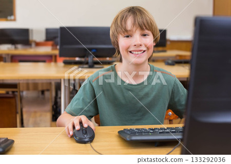 Male child student smiling while using desktop computer and wired mouse at school computer lab desk Male child student smiling while using desktop computer and wired mouse at school computer lab desk 133292036