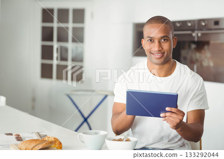 African American man using tablet at kitchen counter with croissant and cereal bowl, copy space 133292044
