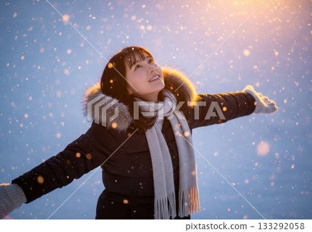 A Japanese woman looks up at the sky in the warm light shining through a snowy field at dusk A Japanese woman looks up at the sky in the warm light shining through a snowy field at dusk 133292058
