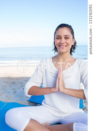 Woman meditating cross-legged on blue yoga mat on sandy beach by calm ocean waves, copy space 133292091