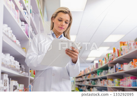 Female pharmacist standing in pharmacy aisle holding clipboard while reviewing medicine bottles Female pharmacist standing in pharmacy aisle holding clipboard while reviewing medicine bottles 133292095