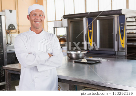 Senior male chef wearing jacket crossing arms in bakery beside steel worktable, copy space Senior male chef wearing jacket crossing arms in bakery beside steel worktable, copy space 133292159