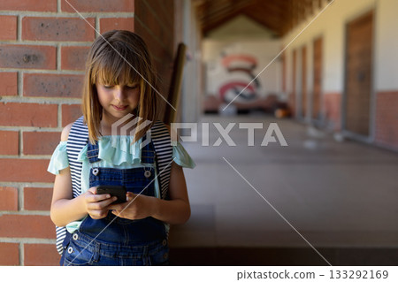 Female child using smartphone leaning on brick pillar in school hallway with backpack, copy space Female child using smartphone leaning on brick pillar in school hallway with backpack, copy space 133292169