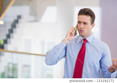 Businessman wearing red tie gesturing on smartphone by glass railing stairs in office, copy space 133292172