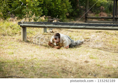 Male soldier wearing camouflage uniform crawling under netted metal beam on obstacle course Male soldier wearing camouflage uniform crawling under netted metal beam on obstacle course 133292189