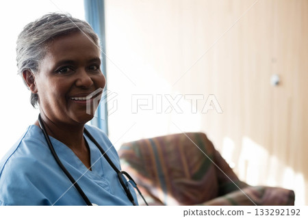 Senior African American nurse smiling while sitting in clinic in scrubs and stethoscope, copy space 133292192