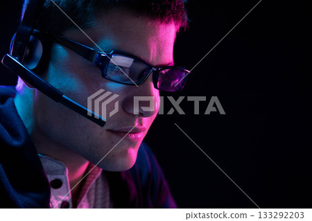 Man wearing eyeglasses and headset with boom microphone focusing on screen in neon room, copy space Man wearing eyeglasses and headset with boom microphone focusing on screen in neon room, copy space 133292203