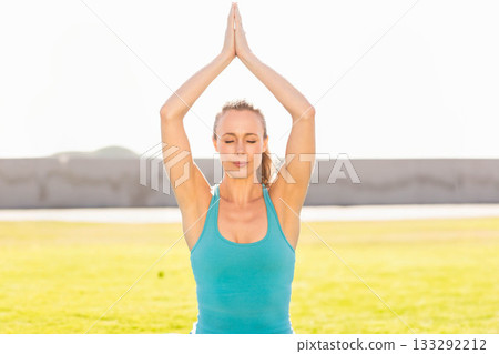 Woman standing on grassy field in yoga prayer pose centering body under bright sunlight 133292212