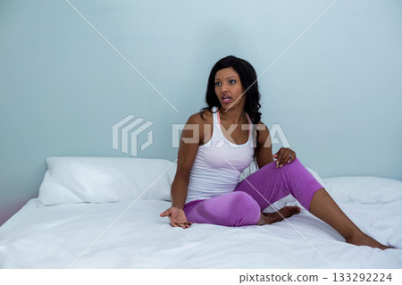 African American woman wearing casual sportswear speaking and gesturing on white bed in bedroom 133292224