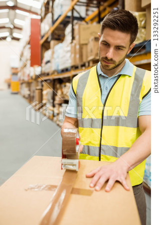 Male warehouse worker sealing cardboard box in warehouse wearing vest, using tape gun, copy space Male warehouse worker sealing cardboard box in warehouse wearing vest, using tape gun, copy space 133292251