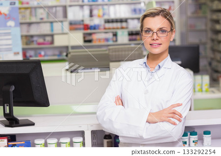 Female pharmacist standing at pharmacy counter, wearing lab coat, facing computer and bottles 133292254