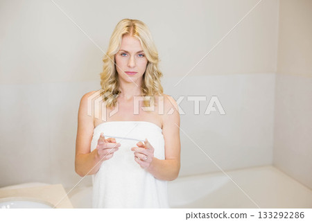 Woman in mid thirties standing in bathroom wrapping towel while holding pregnancy test device 133292286