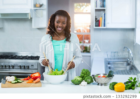 African American woman mixing lettuce in white bowl on kitchen island using wooden salad spoons African American woman mixing lettuce in white bowl on kitchen island using wooden salad spoons 133292299