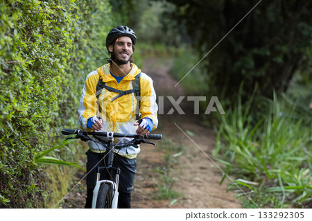 Man holding white mountain bike handlebars while standing on forest path wearing yellow windbreaker 133292305