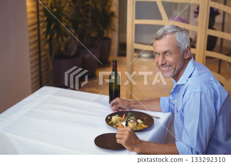 Senior man holding fork and knife at restaurant table with plated meal and wine, copy space 133292310