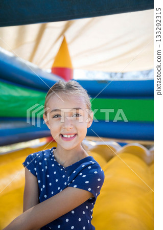 Girl standing in front of inflatable slide at outdoor play zone wearing navy polka dot shirt Girl standing in front of inflatable slide at outdoor play zone wearing navy polka dot shirt 133292315