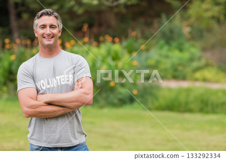 Male volunteer folding arms in jeans and volunteer T-shirt on lawn near orange flowers, copy space 133292334