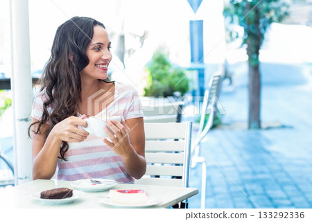 Woman sitting at metal table in sidewalk cafe holding coffee cup, smiling near pastries, copy space Woman sitting at metal table in sidewalk cafe holding coffee cup, smiling near pastries, copy space 133292336