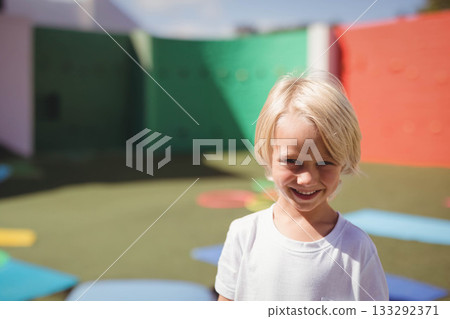 Smiling blond boy wearing white T-shirt on playground with foam mats, climbing holds, copy space Smiling blond boy wearing white T-shirt on playground with foam mats, climbing holds, copy space 133292371
