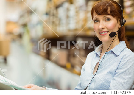 Woman call center agent holding printed documents and speaking into headset mic at desk, copy space 133292379