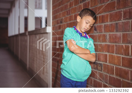 Boy leaning against red brick wall and white railing with arms crossed in corridor, copy space 133292392