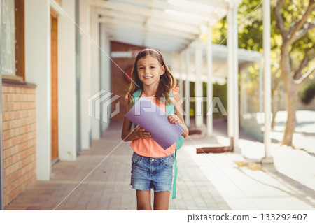 School-aged girl holding purple folder and carrying teal backpack on tiled floor under columns School-aged girl holding purple folder and carrying teal backpack on tiled floor under columns 133292407