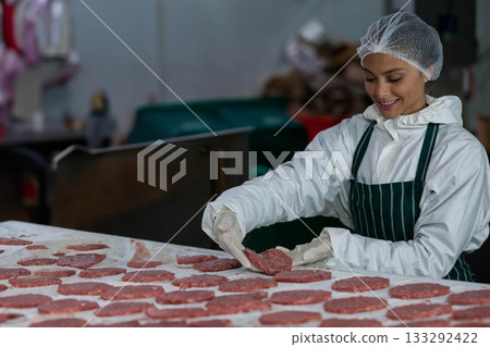 Female processing operator arranging burger patties on stainless steel table in plant, copy space 133292422