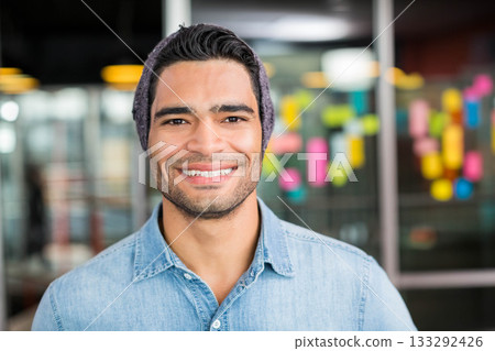 Man in his 30s standing in office smiling at camera by glass partition with sticky notes 133292426