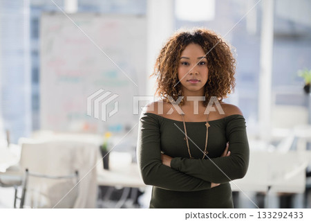 African American woman standing with arms crossed in meeting space near whiteboard and potted plant 133292433