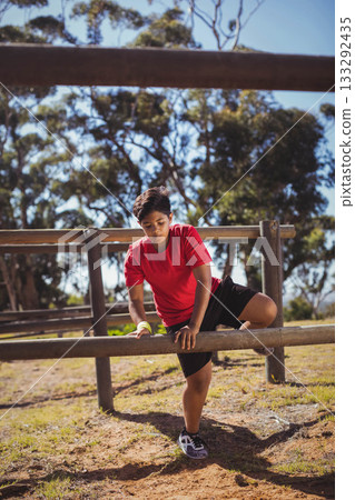Male child climbing over wooden fence at park wearing red T-shirt yellow wristband sneakers Male child climbing over wooden fence at park wearing red T-shirt yellow wristband sneakers 133292435