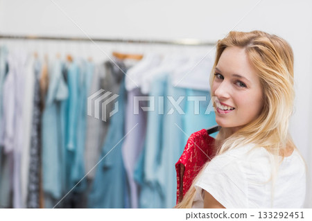 Blonde woman holding red lace top while browsing clothing rack at boutique, copy space Blonde woman holding red lace top while browsing clothing rack at boutique, copy space 133292451