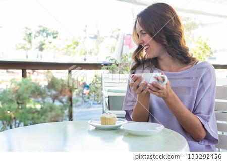 Smiling woman in lavender top sitting at outdoor café holding coffee mug with cupcake, copy space Smiling woman in lavender top sitting at outdoor café holding coffee mug with cupcake, copy space 133292456